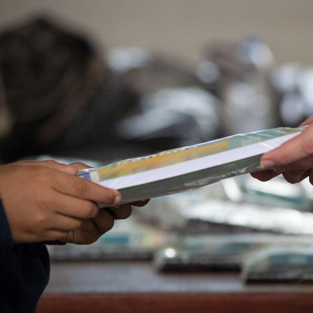 manos de un adulto entregando cuadernos a niño
