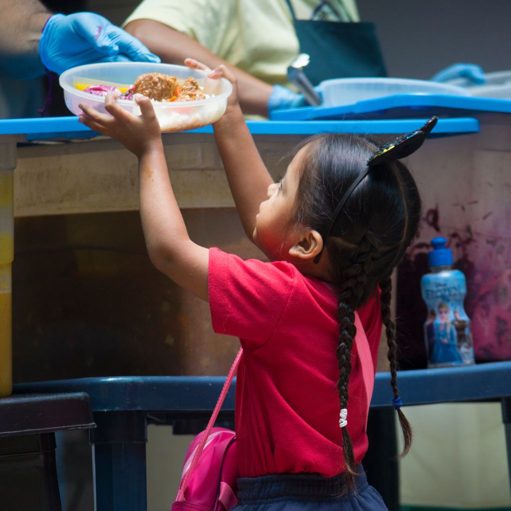 niña pequeña recibiendo envase con comida
